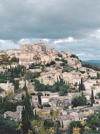 Buildings in town on top hill against cloudy sky