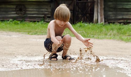 Full length of shirtless boy playing with muddy water