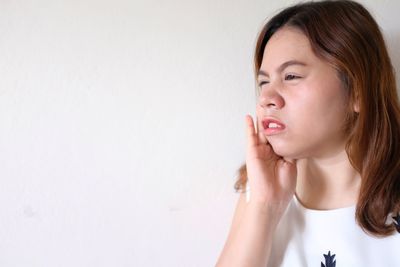 Young woman suffering from toothache against white wall