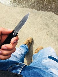 Low section of man holding knife while standing on footpath