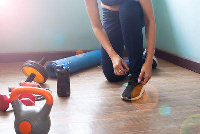 Low section of woman tying shoelace on hardwood floor at home