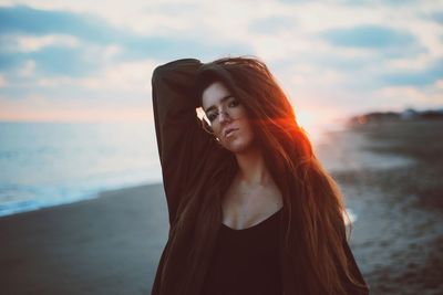 Portrait of young woman standing at beach during sunset