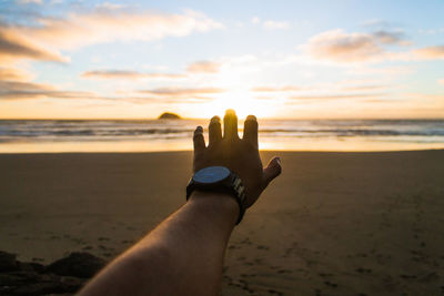 Low section of person on sand at beach against sky during sunset