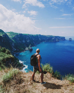 Rear view of man standing on cliff by sea