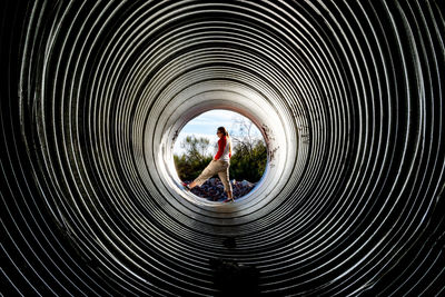 Woman standing in huge metallic pipe