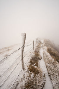 Fence on snow covered landscape against sky