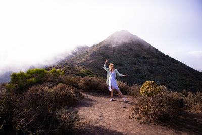 Rear view of woman with arms raised on mountain against sky