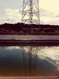 Reflection of electricity pylon on lake against sky during sunset