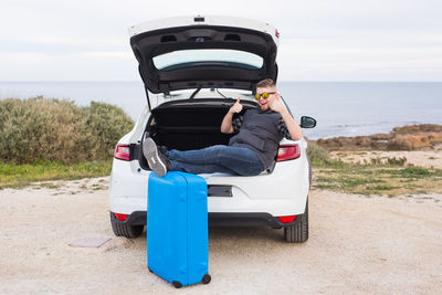 Rear view of man in car by sea against sky