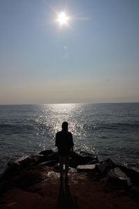 Rear view of man standing on rock by sea against sky