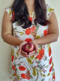 Midsection of woman holding apple while standing against wall