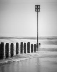 Wooden posts in sea against clear sky