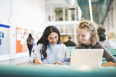 Smiling young female students studying in cafeteria at university