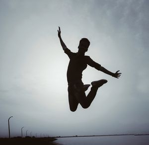Low angle view of silhouette man jumping against sky