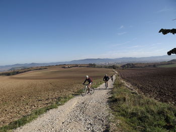 Men riding bicycles on dirt road against blue sky