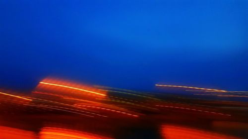 Illuminated light trails against clear blue sky at night