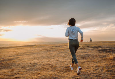 Rear view of woman standing on field against sky during sunset