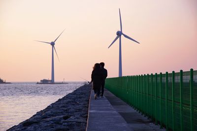 Rear view of man standing on shore against sky during sunset