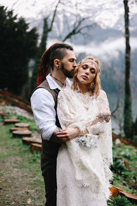 Two happy people in love the bride and groom in wedding outfits embrace by the lake and mountains