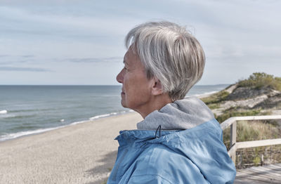 Side view of young woman standing at beach against sky