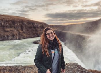 Portrait of smiling young woman standing against sky during sunset