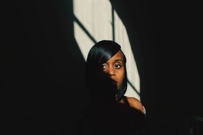 Portrait of beautiful young woman standing in dark room