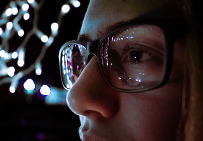 Close-up of teenage girl wearing eyeglasses reflecting illuminated lights
