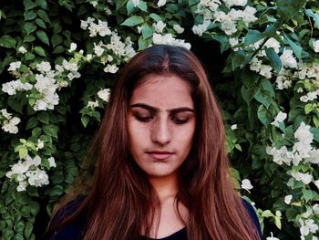 Beautiful young woman looking down while standing against plants