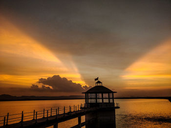 Silhouette built structure by sea against sky during sunset