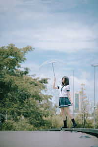 Woman holding umbrella standing by plants against sky