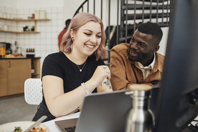 Male computer programmer discussing while looking at happy female colleague in tech start-up office