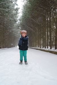 Full length portrait of boy standing on snow covered field amidst bare trees