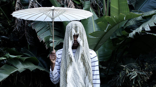 Man with white umbrella wearing scarf against banana tree