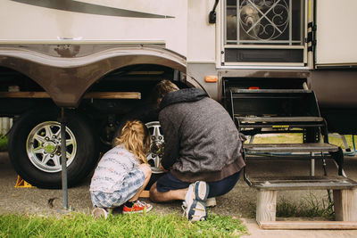 Rear view of father and daughter fixing tire