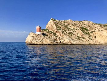 Lighthouse by sea against clear blue sky