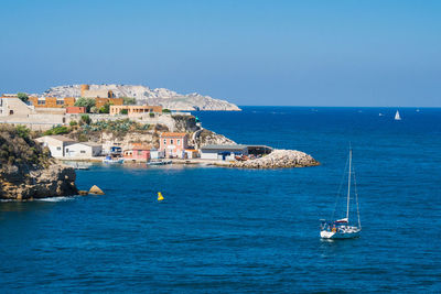 Sailboats in sea by buildings against clear blue sky