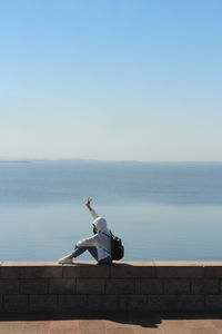 Rear view of woman sitting on retaining wall against aswan dam in a sunny day, egypt