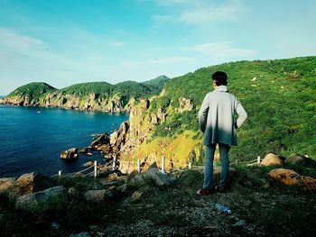 Rear view of man standing on rock against sky