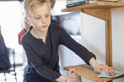 Boy cleaning shelf in house