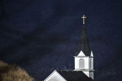 Low angle view of cross amidst buildings against sky