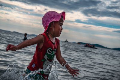 Girl wading in sea against sky during sunset