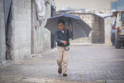 Little refugee children with umbrella in the rain, refugee with umbrella.