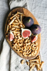 Wine appetizers namely ripe figs, cashews, and salty bread sticks on the table indoors.