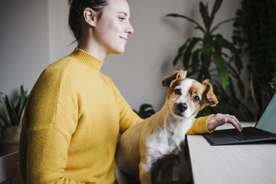 Young woman working on digital tablet while sitting with pet at home office