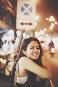 Portrait of young woman smiling while illuminated in city at night