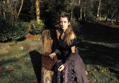 Portrait of young woman sitting on seat in forest