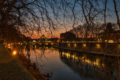 Scenic view of river by illuminated buildings against sky during sunset