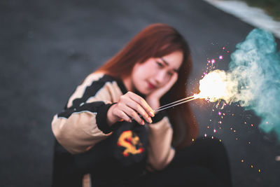 Young woman holding sparklers while sitting outdoors