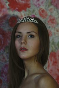 Close-up of beautiful woman wearing tiara against floral wallpaper