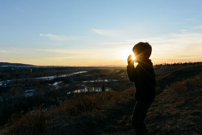 Rear view of man standing on field against sky during sunset